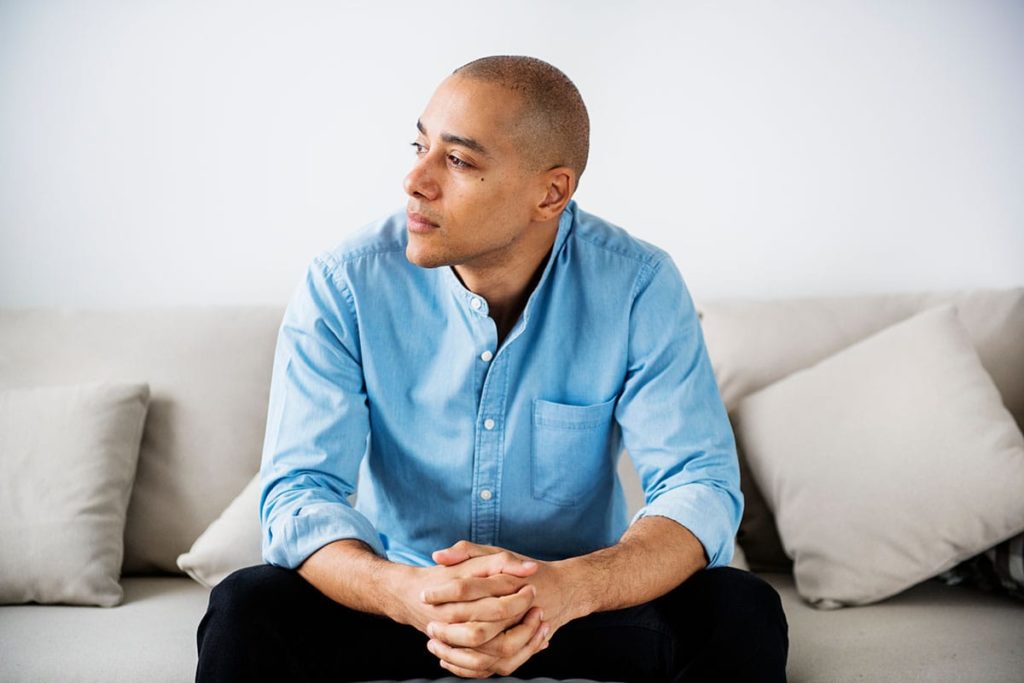 person on couch in denim shirt considering the signs of alcoholism
