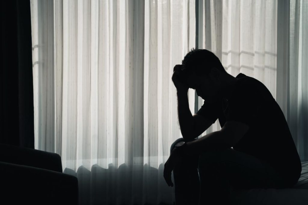 man by window with head in hands considers the long-term effects of heroin