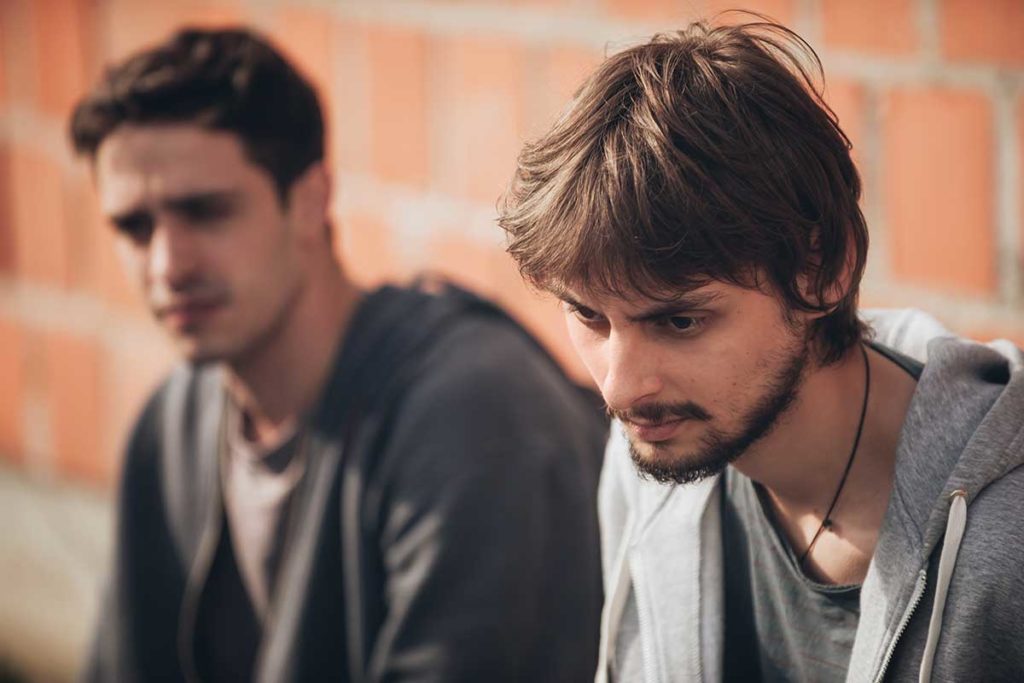 man in grey sweatshirt talks with friend about the signs of cocaine addiction