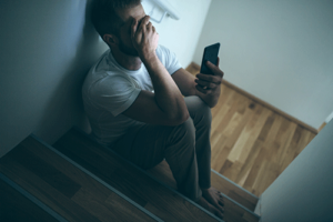 man sits on floor and looks at phone cosidering a depression treatment program in north carolina
