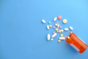 Colorful pills spilling out of an orange RX bottle onto a blue background.