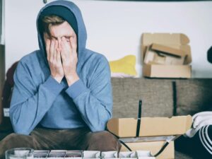 A tired man in a blue hoodie rubs face with his hands while looking for crack addiction treatment.