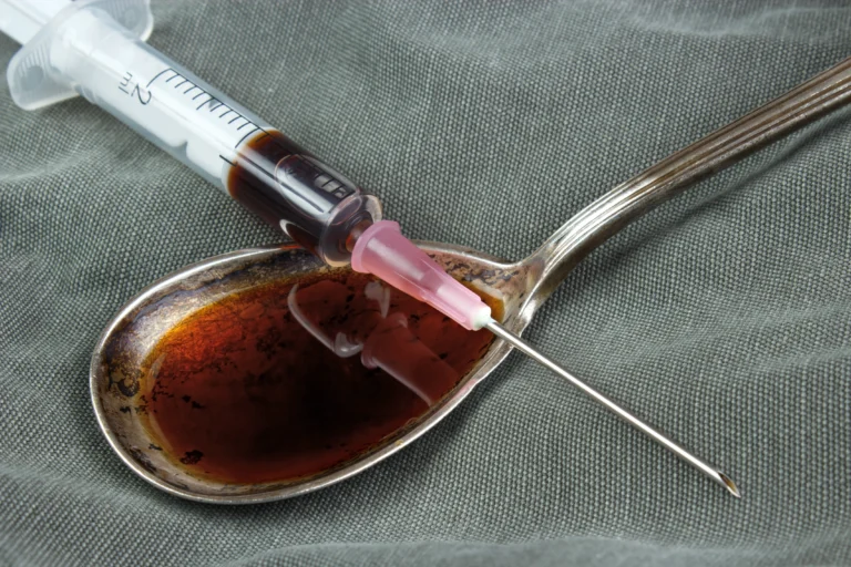 liquid form brown heroin in a spoon with a syringe sitting on top of the spoon that is filled with heroin